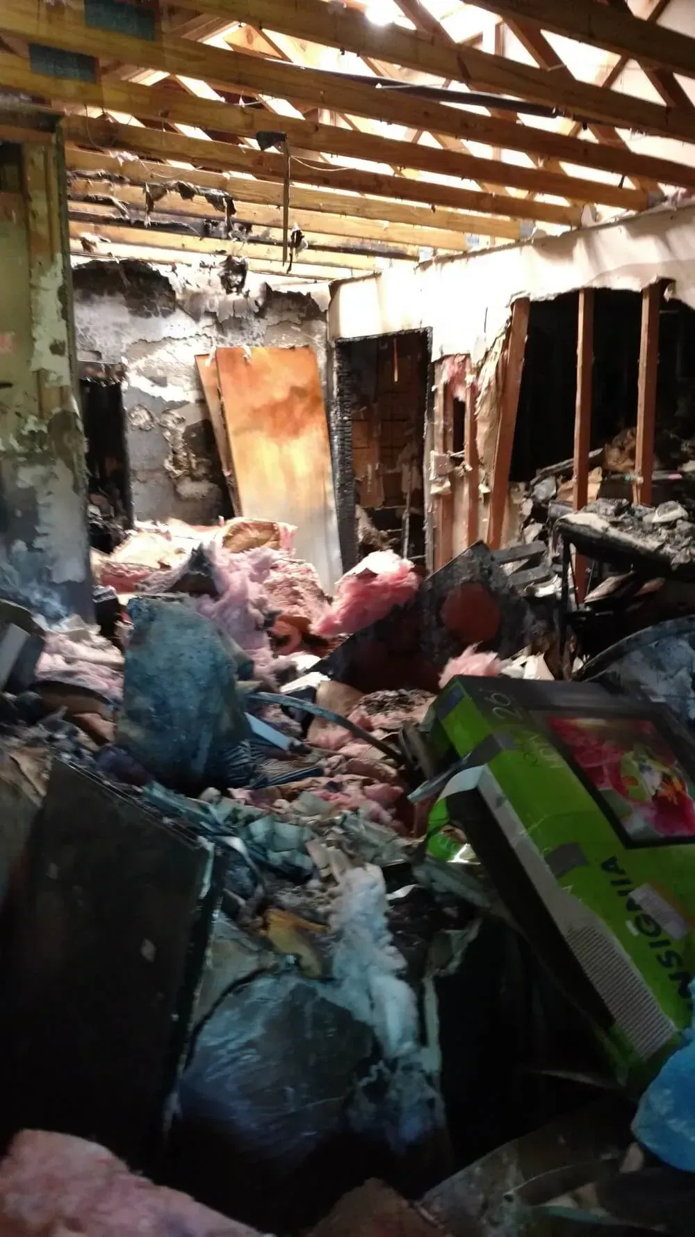 Interior view of a fire-damaged room with debris, exposed beams, and a doorway.
