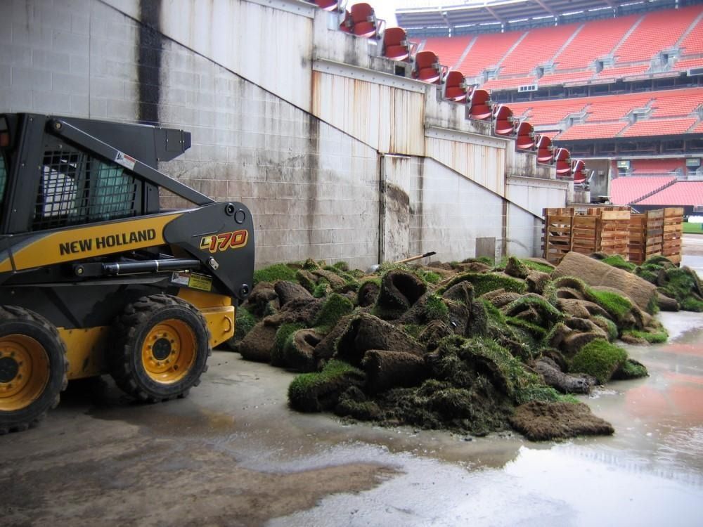 Skid steer next to a pile of sod near a stadium wall.
