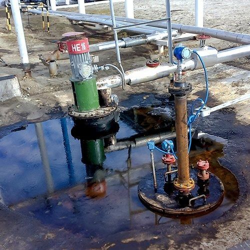 Oil pump equipment in a shallow puddle, near pipes and a metal structure.