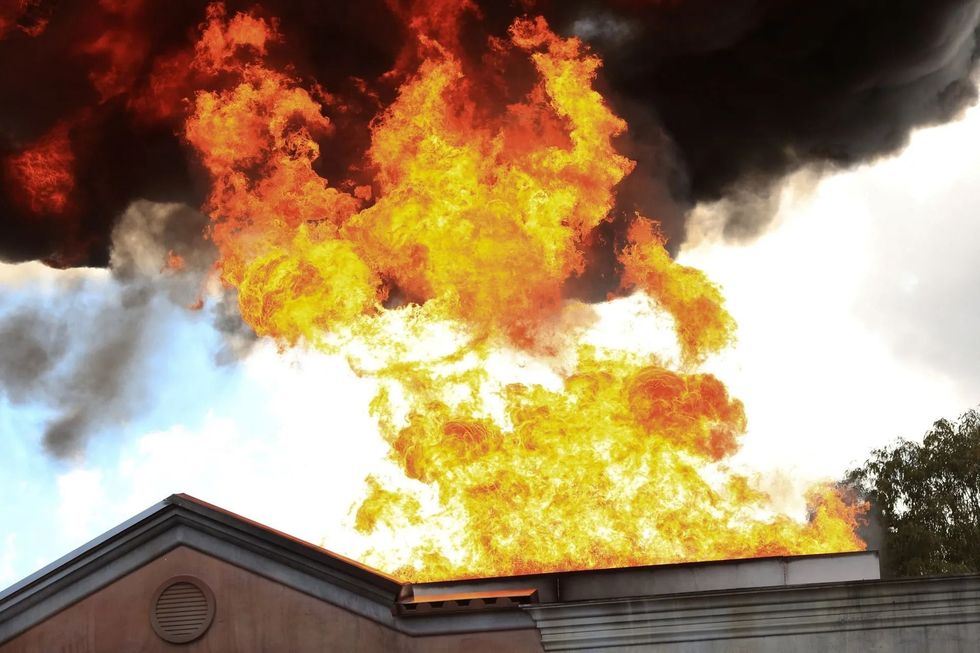 Roof engulfed in flames, thick black smoke billowing into a cloudy sky.