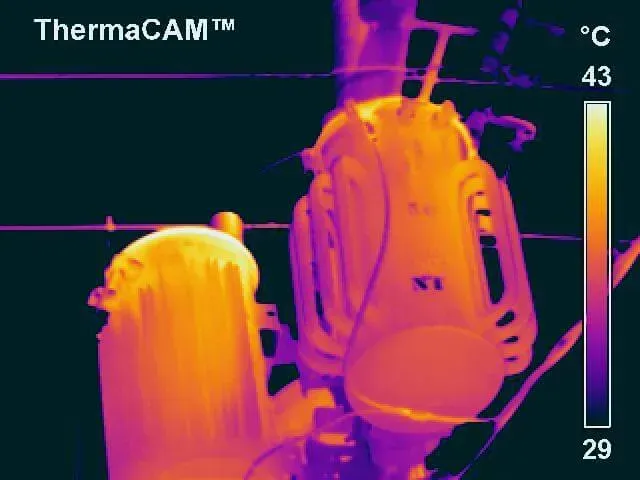 Thermal camera view of electrical transformer, showing heat distribution in shades of yellow and orange.