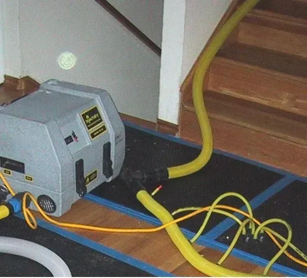 Gray dehumidifier with yellow hoses on a mat near stairs.
