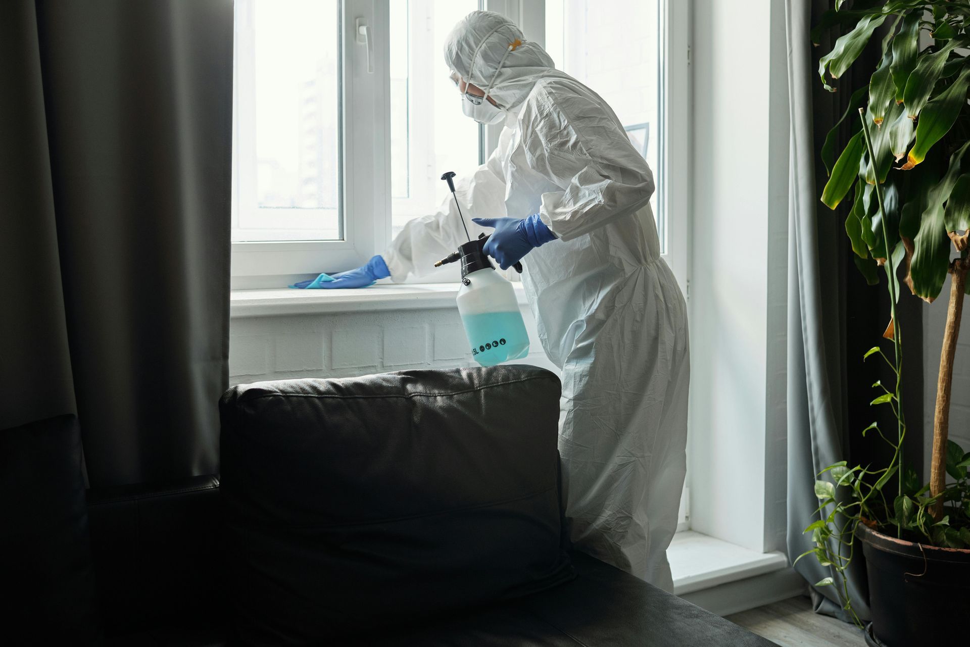 Person in hazmat suit disinfecting a window sill with a spray bottle.