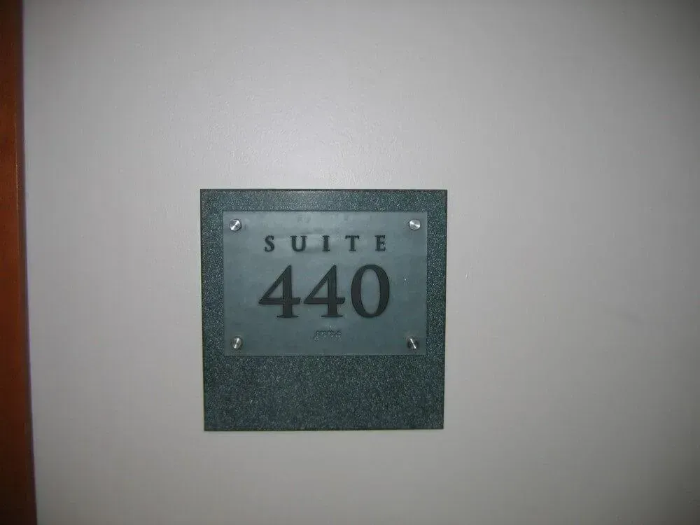 Suite 440 sign on a speckled dark green background, mounted on a light gray wall.