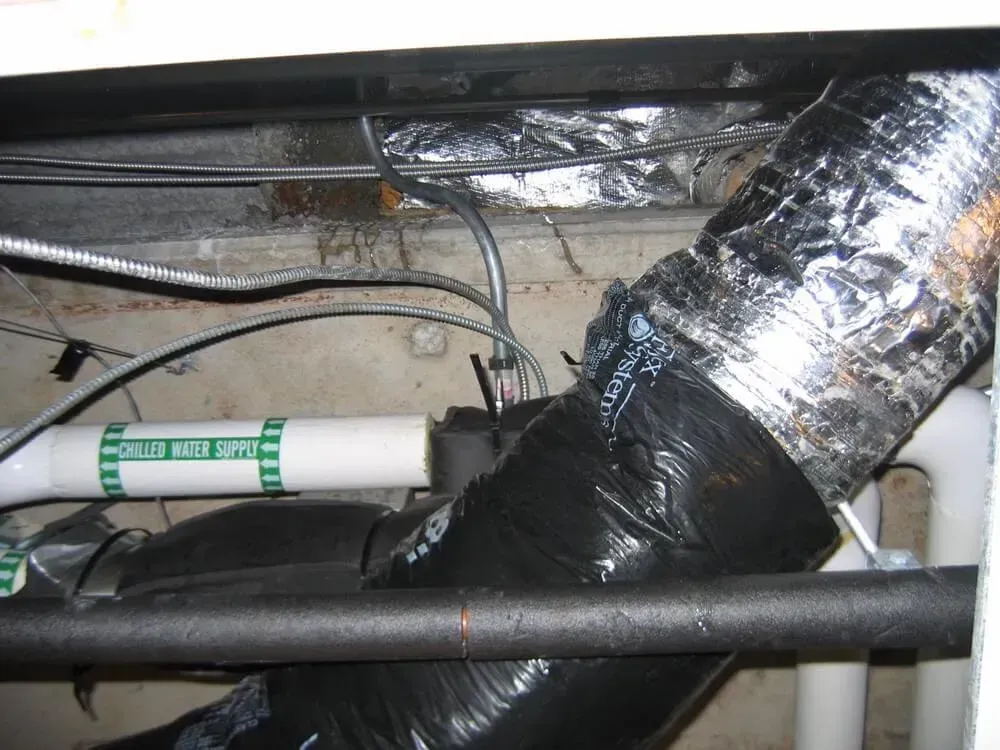 HVAC ductwork with black insulation tape, PVC pipes, and electrical wiring in a crawl space.