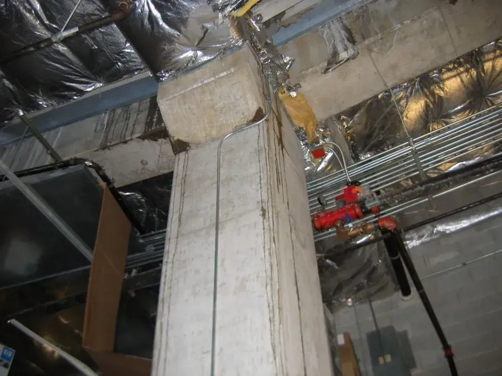 Concrete support column in an industrial setting, with exposed ductwork, pipes, and insulation.