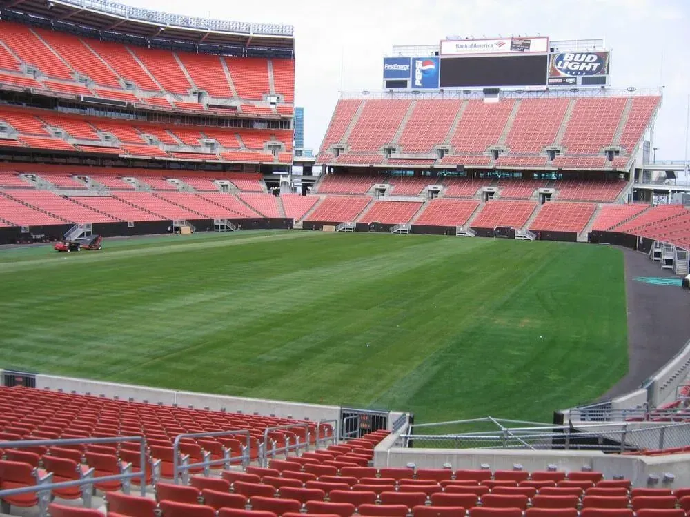 Empty football stadium with red seats and freshly cut green grass.