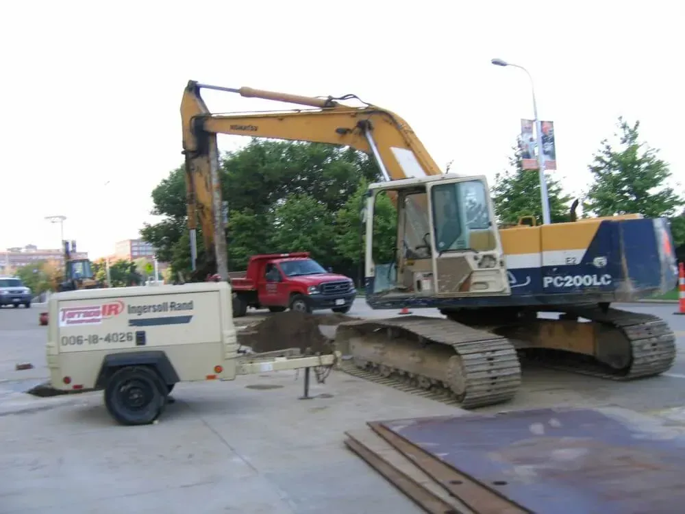 Excavator and trailer on a construction site next to a street. Red truck in the background.