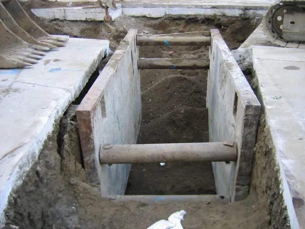 Excavated trench with concrete walls supported by steel bars; construction site.