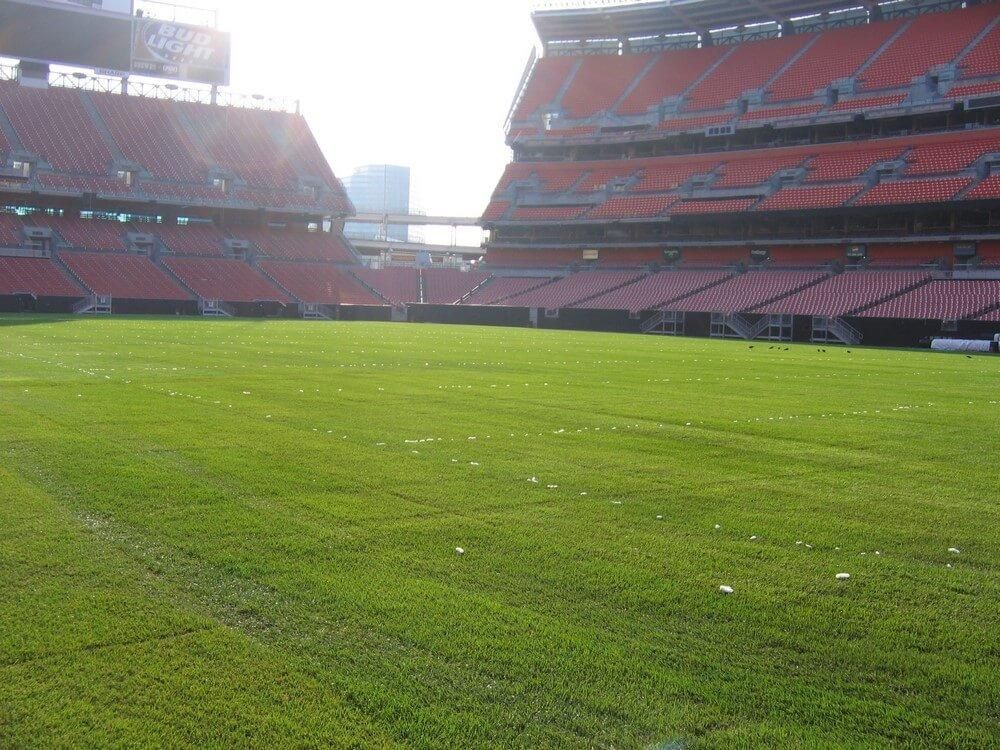 Empty football field in stadium with brown seating, bright green grass.