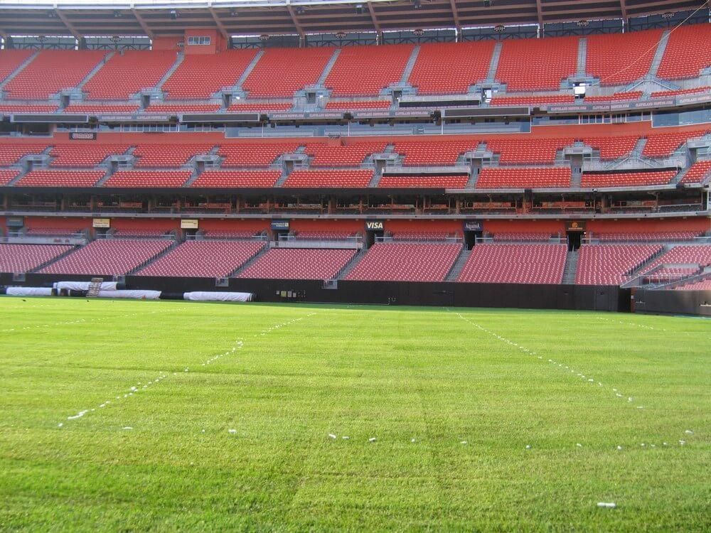 Empty orange stadium seats overlooking a green grass field.