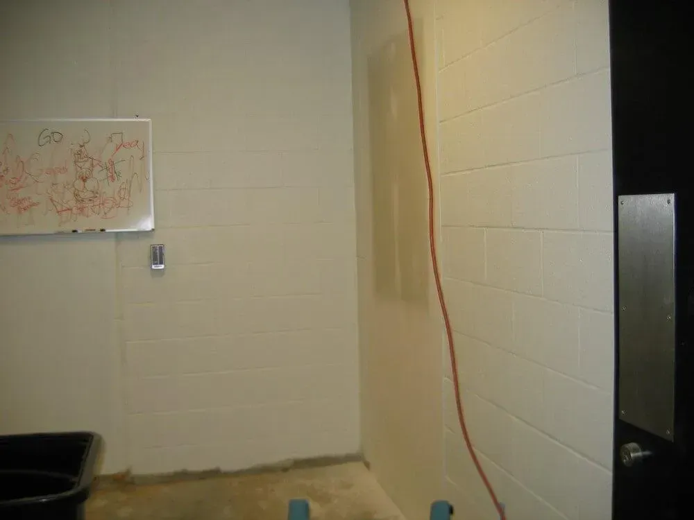 White block walls with a red electrical cord running vertically. A whiteboard is on the left wall.
