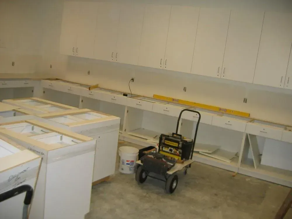 Kitchen cabinets in various stages of installation; tools and construction materials. White cabinets.