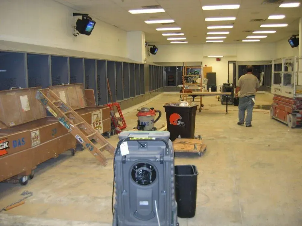 Interior view of a locker room under construction; brown crates, tools, and a worker visible.