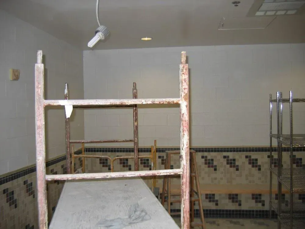 Scaffolding in a room with tiled walls; overhead lighting visible.