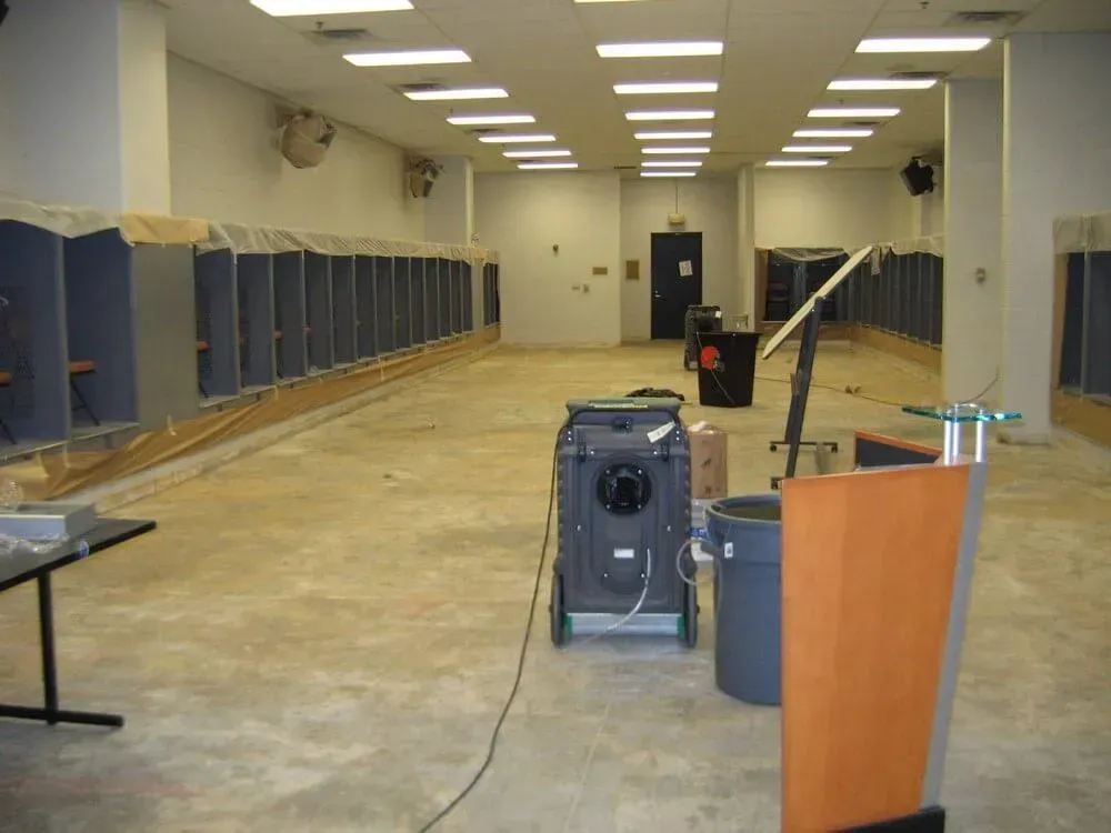Empty room with cubicles along the walls, a floor machine, and a podium; construction or renovation is in progress.