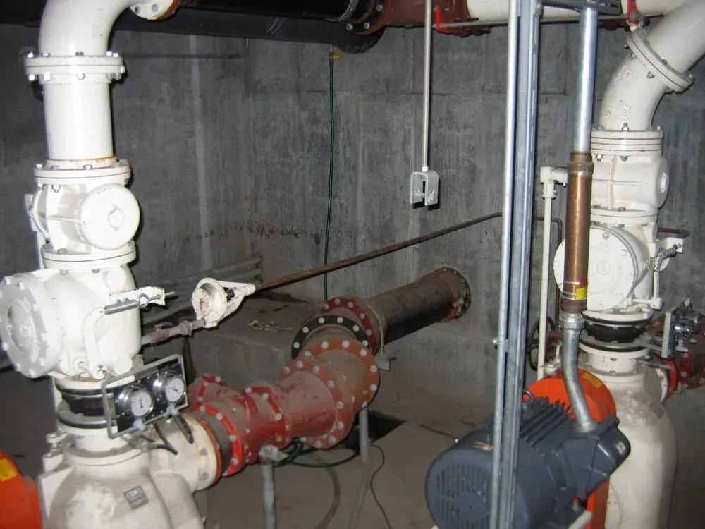 Industrial pipes and pumps in a concrete room. Red and white pipes with motors and gauges.