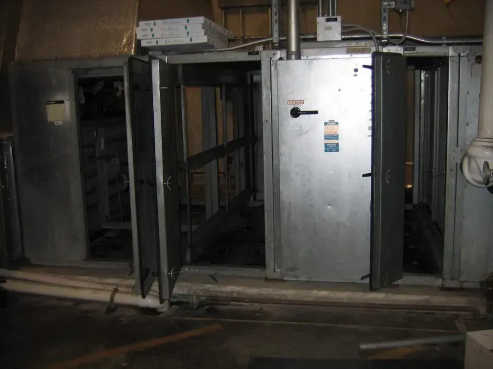 Large industrial HVAC unit with multiple open metal doors in a concrete room.