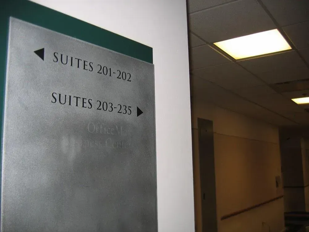 Sign showing suite numbers, direction arrows, and a hallway with a ceiling light.