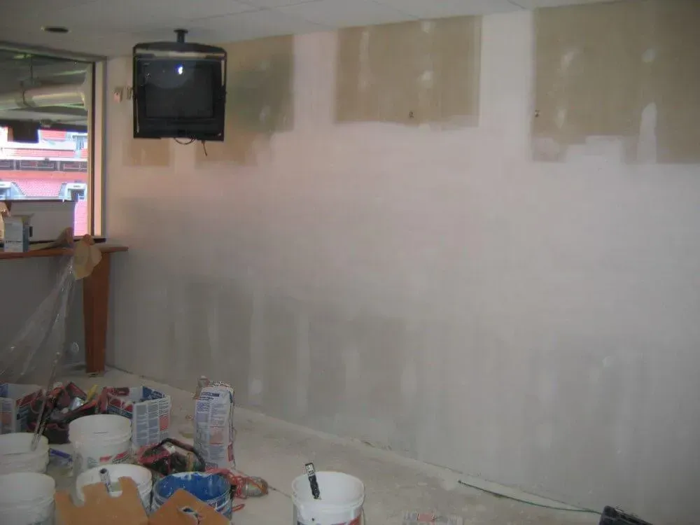 Interior wall with patches of drywall compound, a mounted TV, and construction materials on the floor.