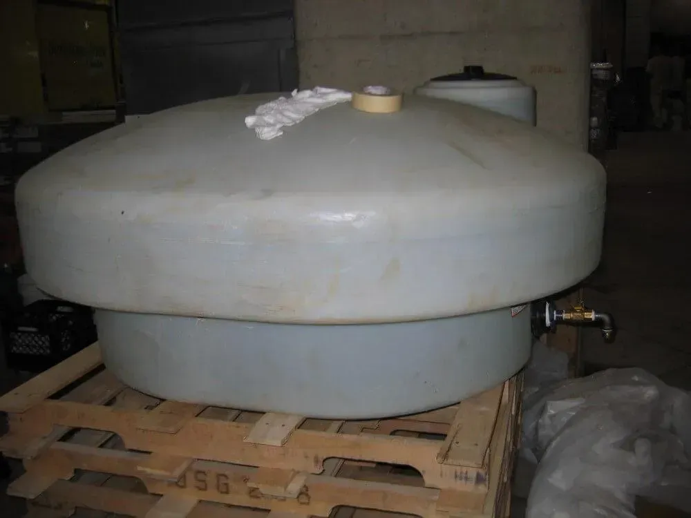 Large, light gray plastic water tank on a wooden pallet, with a spigot and top access port, in an industrial setting.