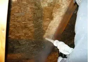 A person spraying insulation into a wall within a wood-framed structure.