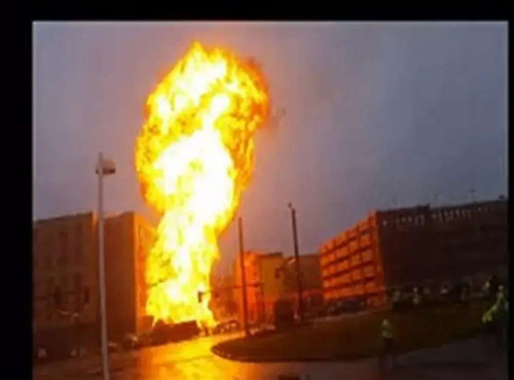 Large explosion erupts in a city, flames engulf buildings, overcast sky.