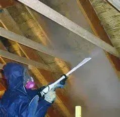 Person in protective gear spraying insulation in an attic.