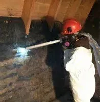Person in protective suit spraying an attic.