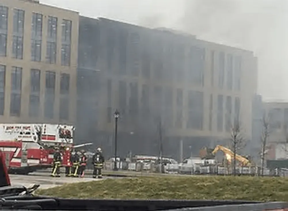 Firefighters at a multi-story building engulfed in smoke. Fire truck and construction equipment visible.