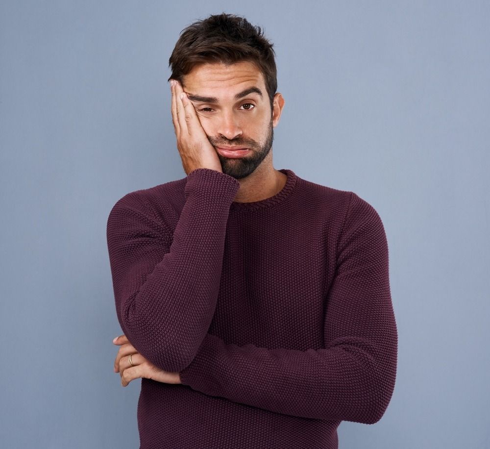 A man in a purple sweater is covering his face with his hand.