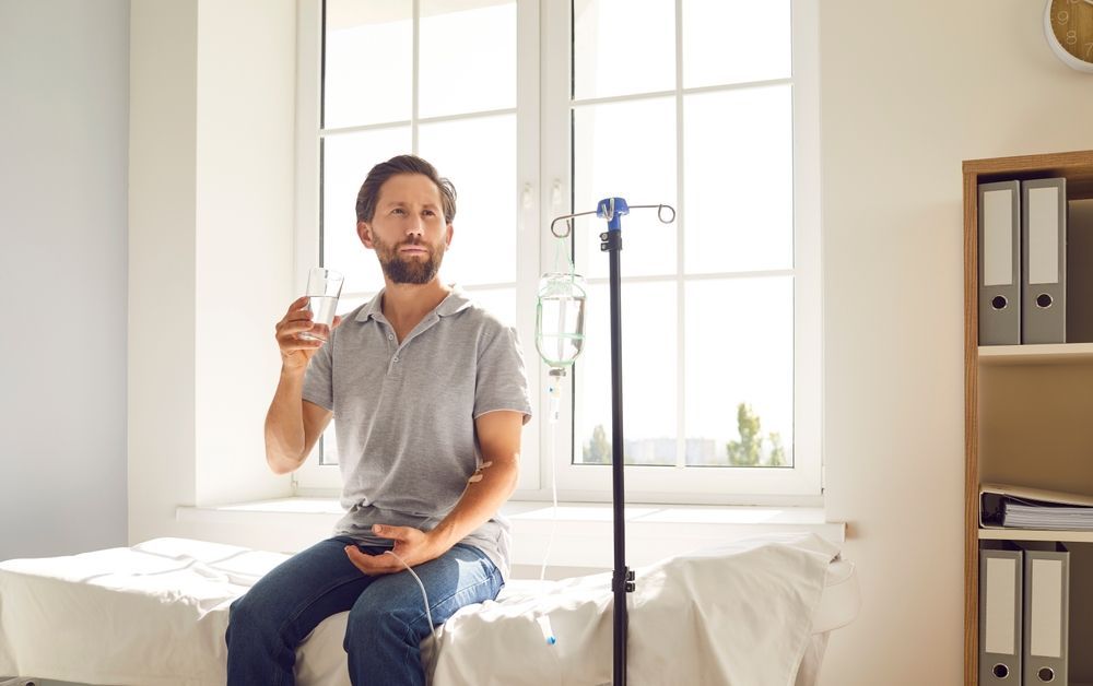 A man is sitting on a bed holding a glass of water.