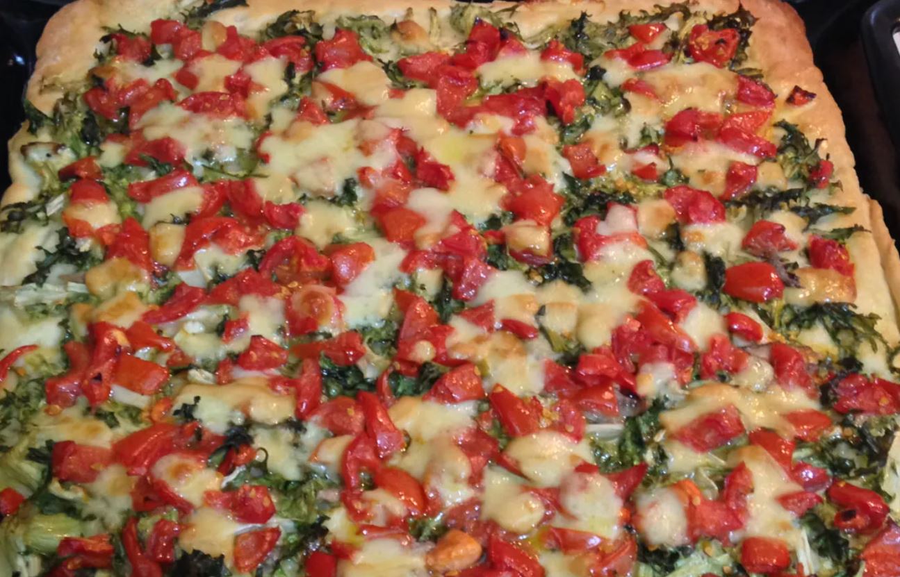 Pizza al forno con pomodori rossi a cubetti e verdure verdi su una crosta dorata.