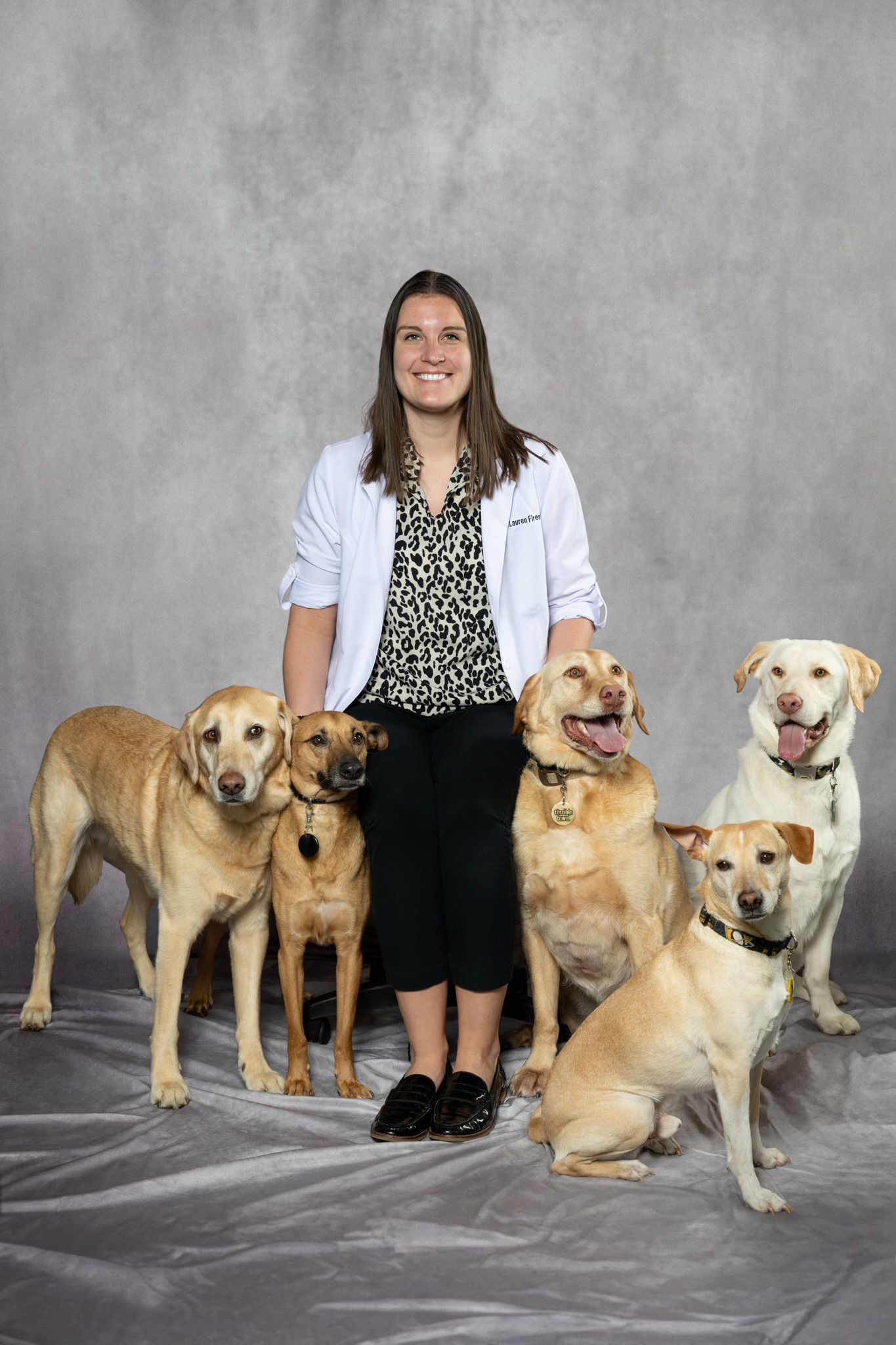 A woman in a white coat is standing next to a group of dogs.