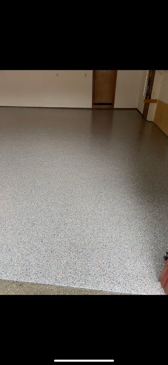 A garage with a gray, speckled epoxy floor. White walls and a wooden door are visible.