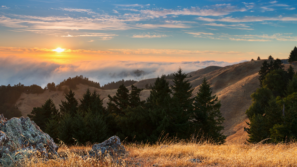 The sun is setting over a mountain covered in fog.