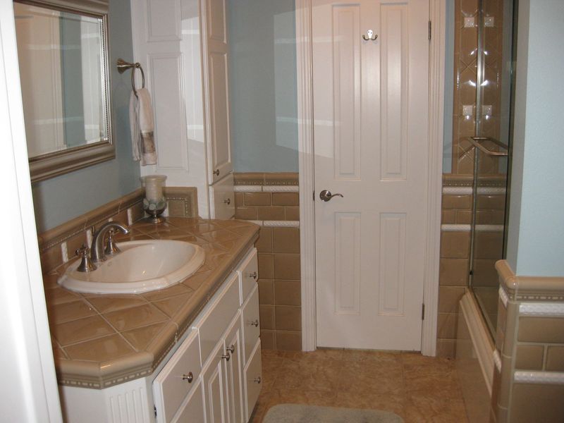 Small beige bathroom with vanity sink, mirror, toilet, tub, and glass shower door.