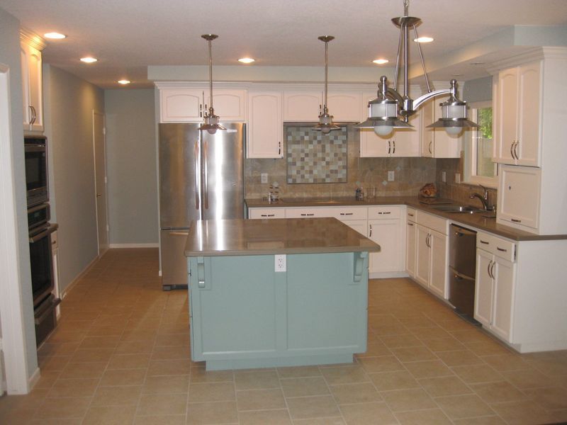 Modern kitchen with white cabinets, stainless steel fridge, and a light blue island with hanging pendant lights