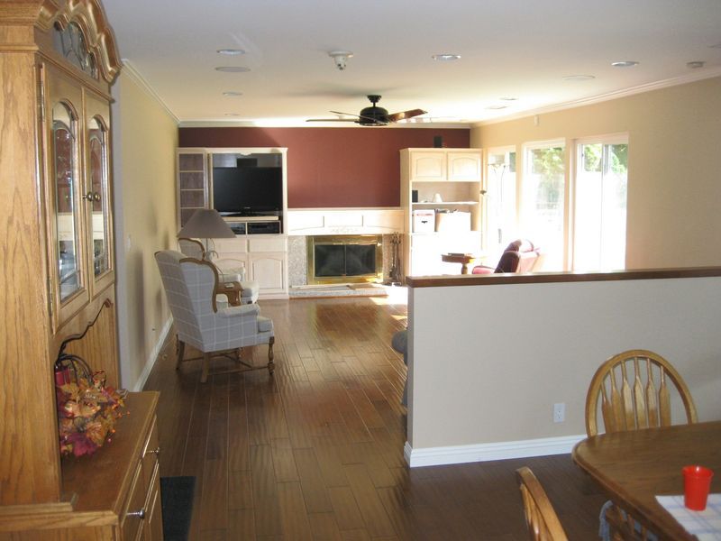 Open-plan living room and kitchen with wood floors, fireplace, dining table, and bright windows