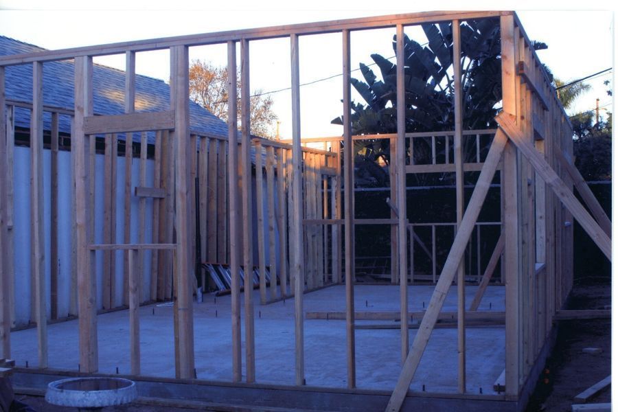 Wood-framed house under construction with exposed studs and open roof framing at dusk
