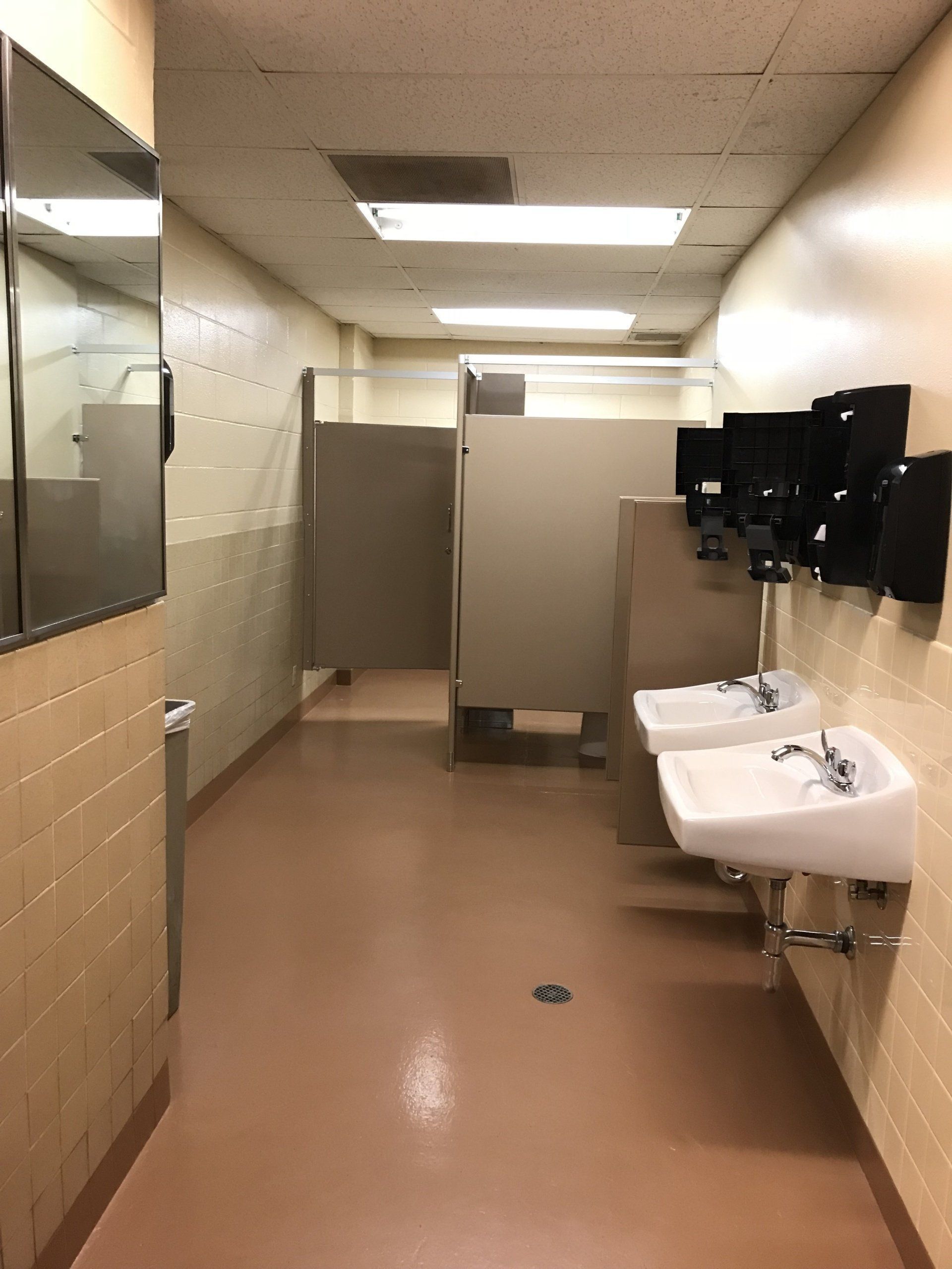 Public restroom with sinks, stalls, and mirrors under fluorescent lights.