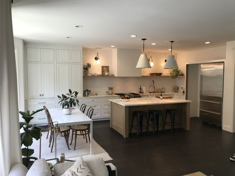 Bright modern kitchen and dining area with island, pendant lights, white cabinets, and dark floors