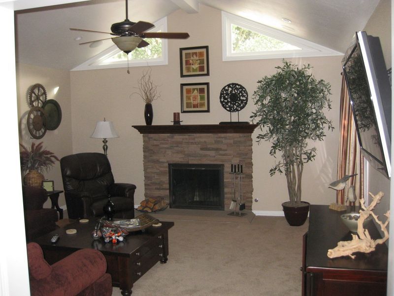 Cozy living room with fireplace, ceiling fan, armchair, coffee table, and potted plant under angled windows