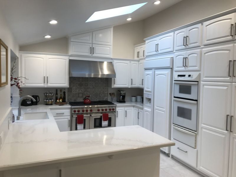 Bright white modern kitchen with island, stainless steel range, built-in ovens, and skylights