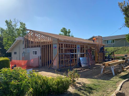 House under construction with exposed framing, scaffolding, and tools in a sunny backyard