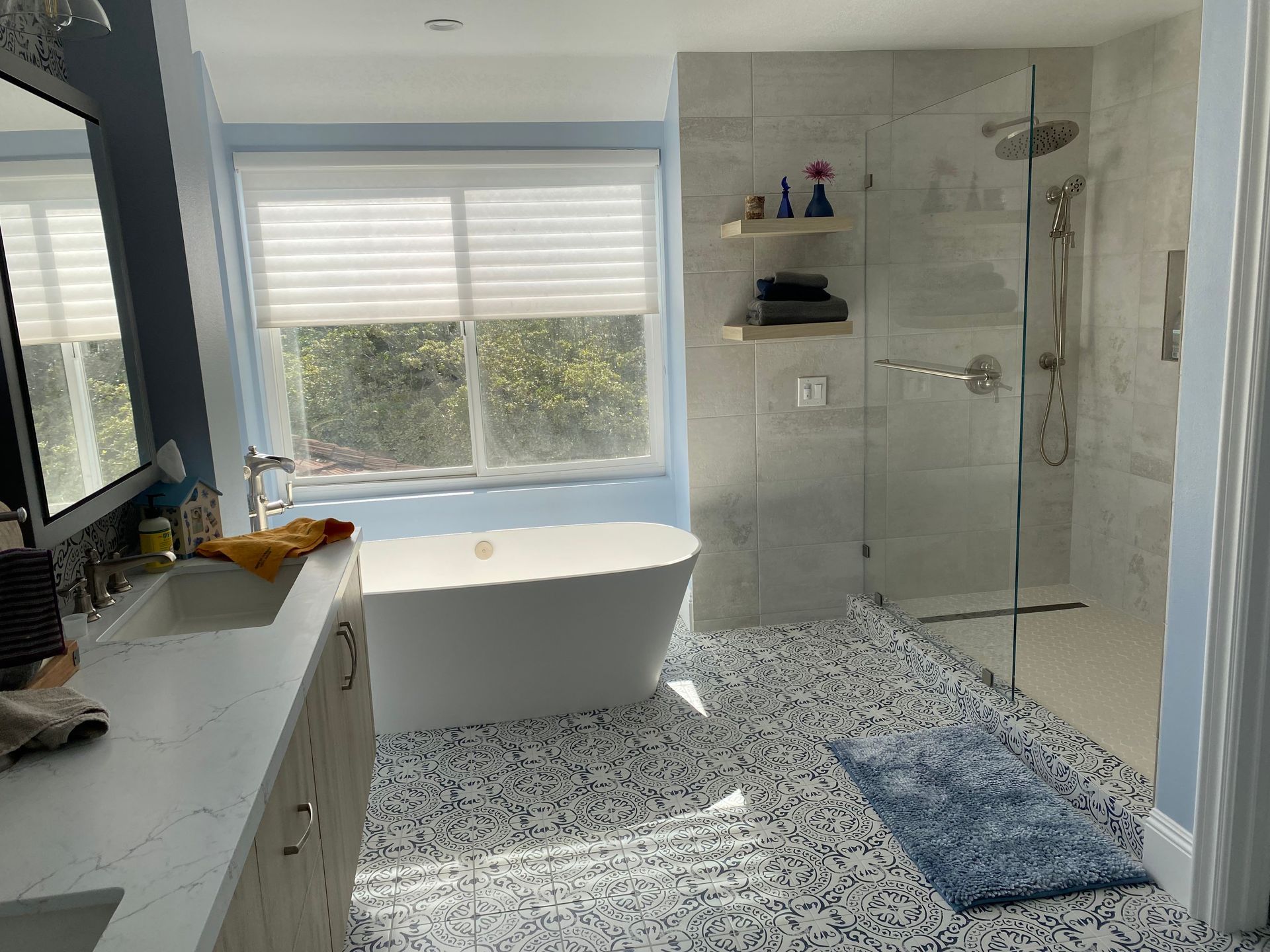 Bright bathroom with freestanding tub, glass shower, white tile, and blue rug by a window.