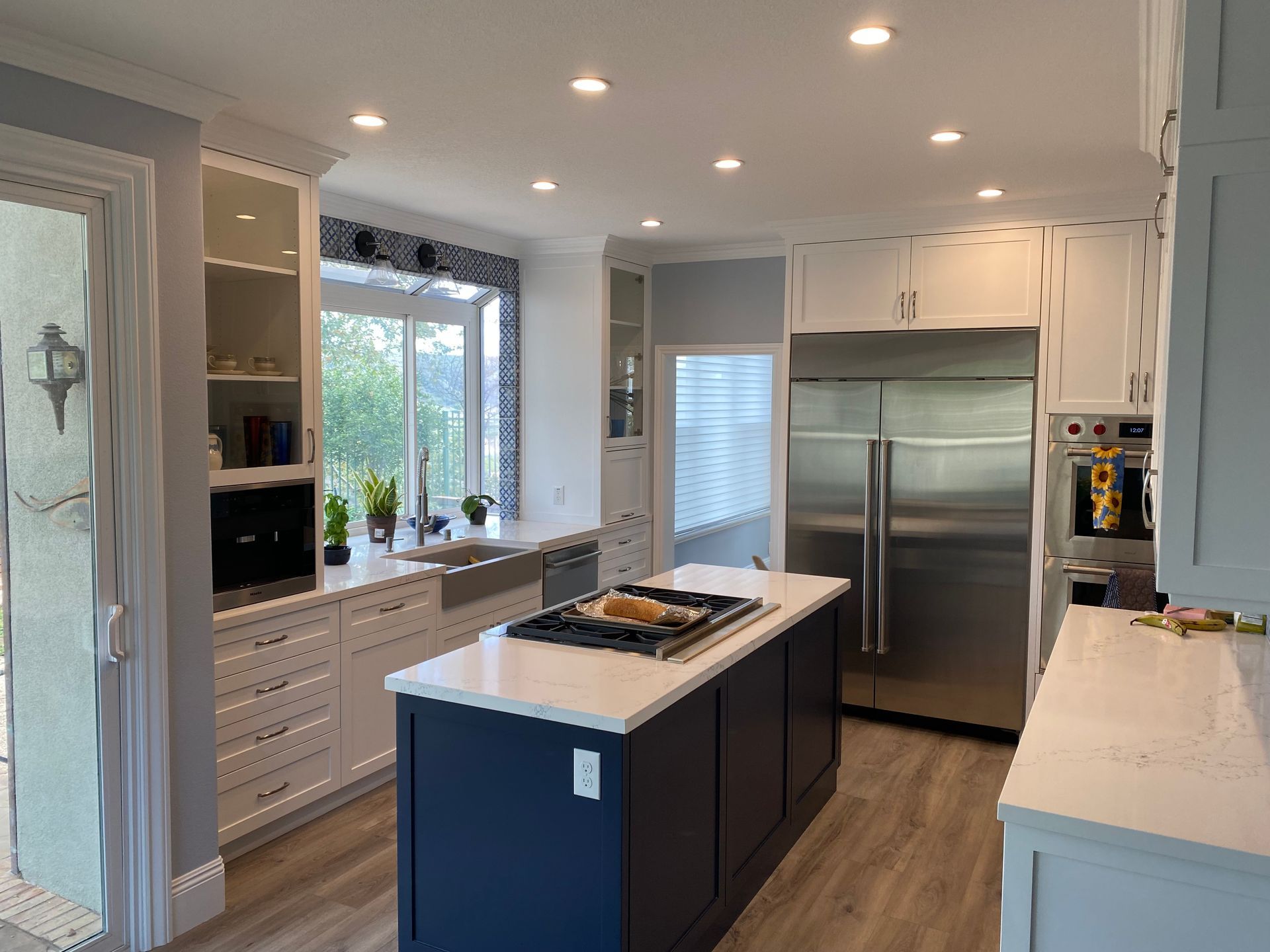 Bright modern kitchen with white cabinets, stainless steel fridge, and navy island under recessed lights