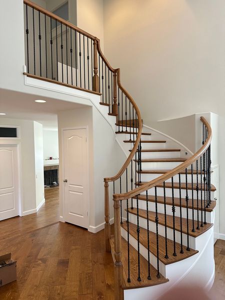 Curved wooden staircase with black balusters and white railing in a bright home interior