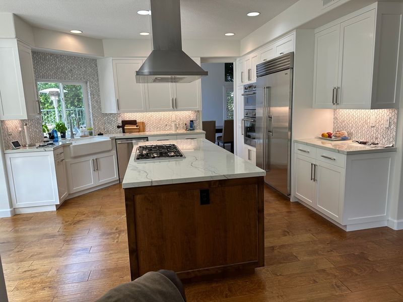 Bright modern kitchen with white cabinets, marble island, stainless appliances, and wood floors