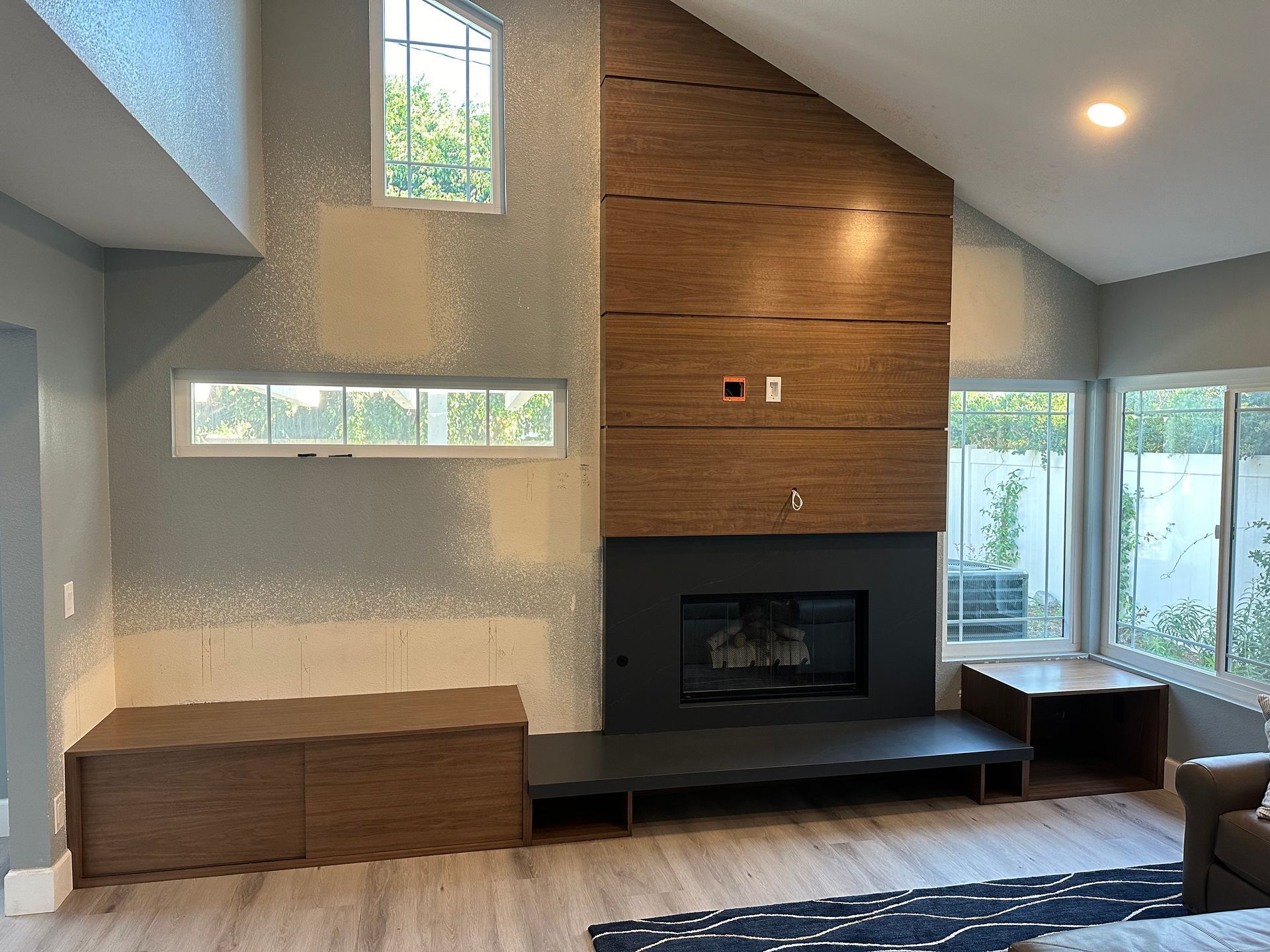 Modern living room with wood-paneled fireplace wall, built-in bench, and tall windows letting in natural light